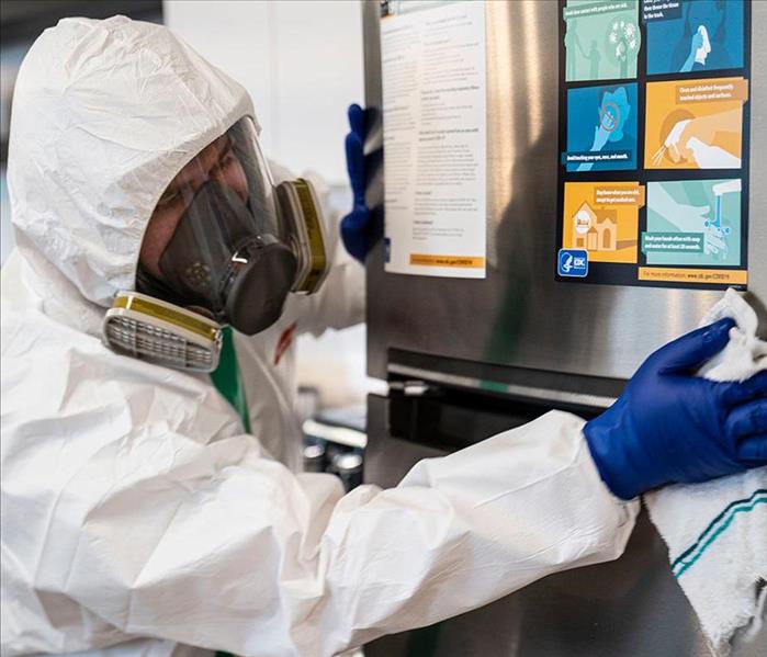 Technician in protective gear wipes fridge